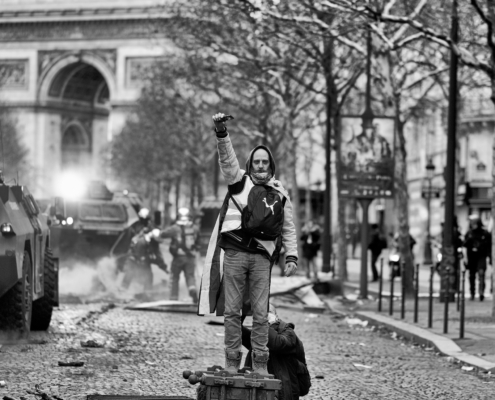 Un manifestant en gilet jaune poing levé avec les pomper et l'Arc de Triomphe au fond