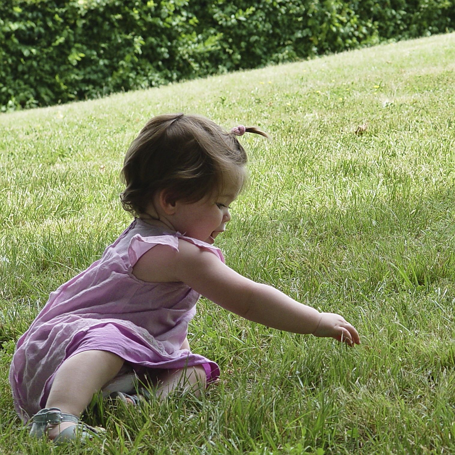 Une toute petite fille habillée en rose qui joue dans l’herbe.